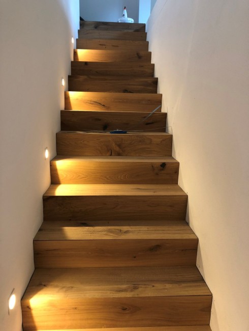 Holztreppe mit Wandlichtern führt nach oben