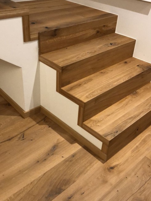 Holztreppe mit hellbrauner Maserung und weißen Wänden